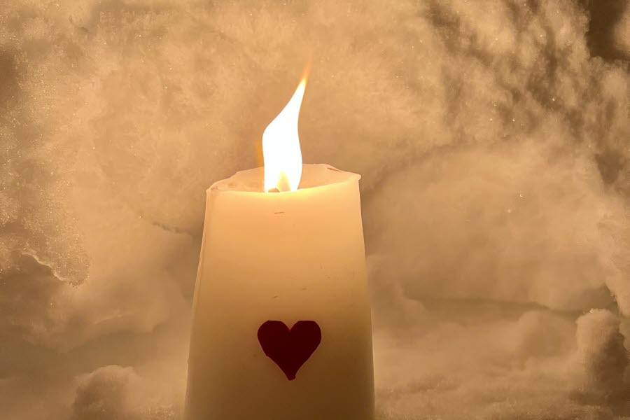 Ett ljus med ett hjärta på som brinner i snön