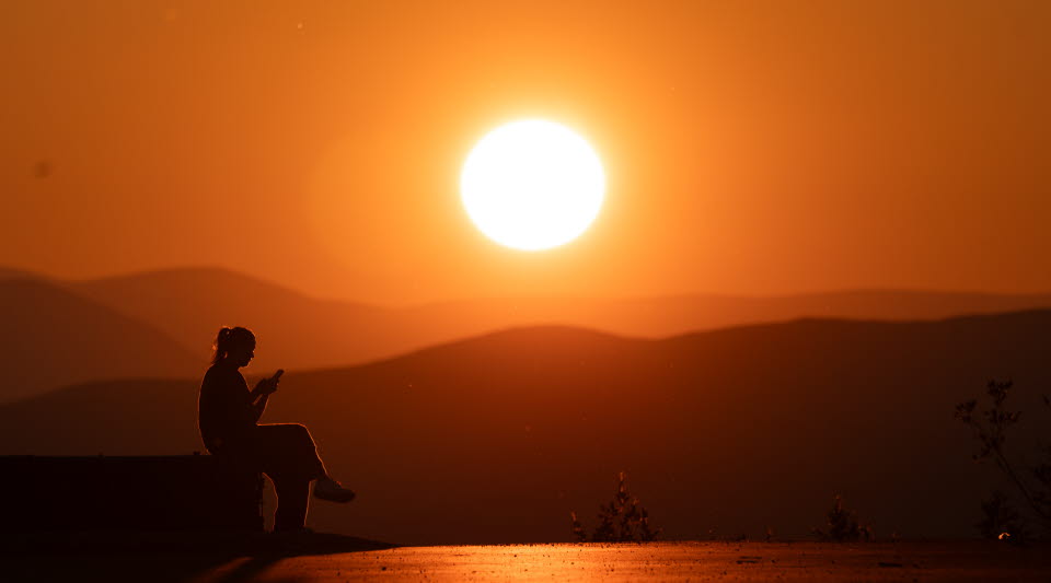 En kvinna som sitter med sin mobiltelefon i solnedgången