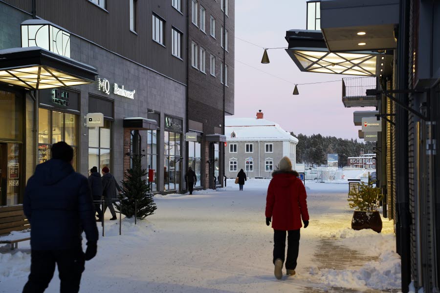Vinterklädd gågata i nya Kiruna centrum med butiker i bottenvåningarna och människor som promenerar mellan husen.