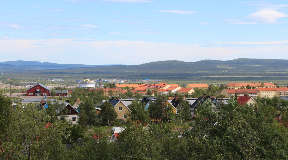 Låga hus omgivna av gröna träd med Kirunas nya stadskärna i horisonten.