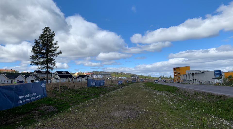 Fotot visar grå villor till vänster, en väg i mitten och till höger gula bostadshus under byggnation. 
