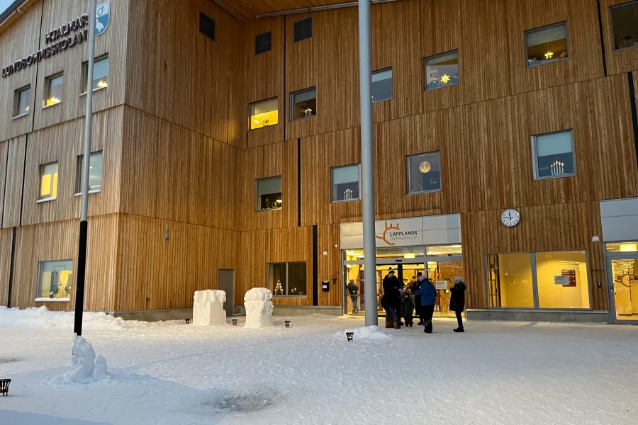 Fotot visar några personer som står utanför en brun byggnad på vintern.