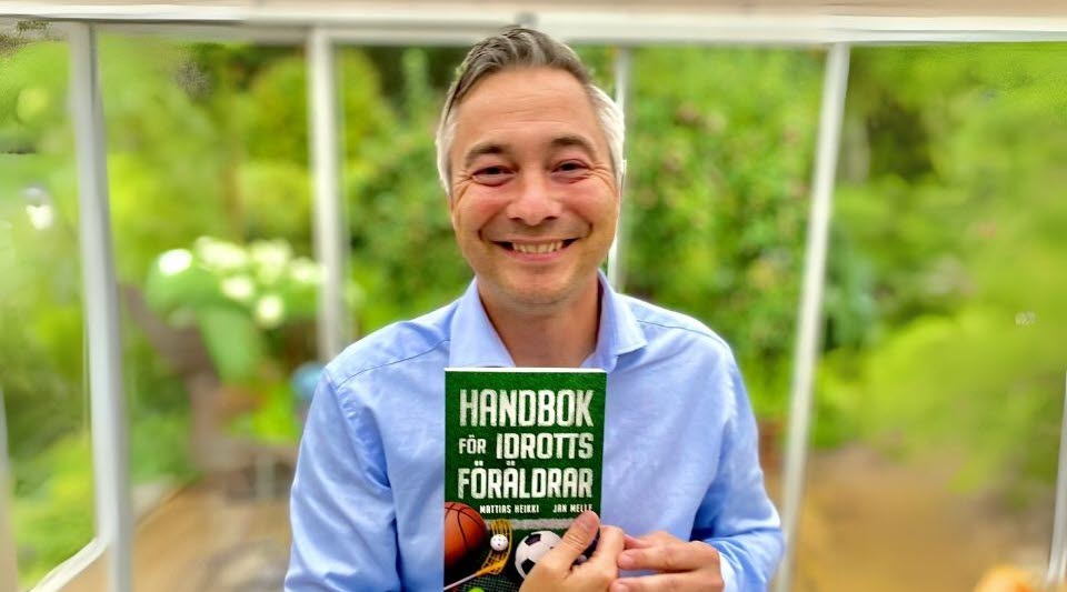 Pressbild av Mattias Heikki med boken "Hanbok för idrottsföräldrar" i handen