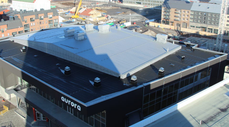 Foto taget högst upp i det nya hotellet visar Aurora kultur och kongress tak och del av framsidan på byggnaden. Runt omkring ses de nya byggnaderna i Kiruna. 