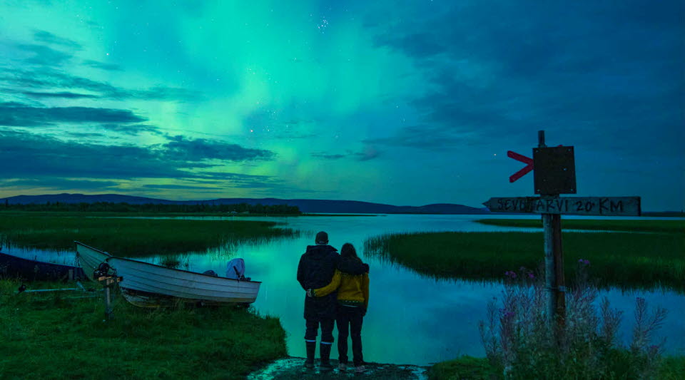 Två personer som håller om varandra vid vattnet under norrsken