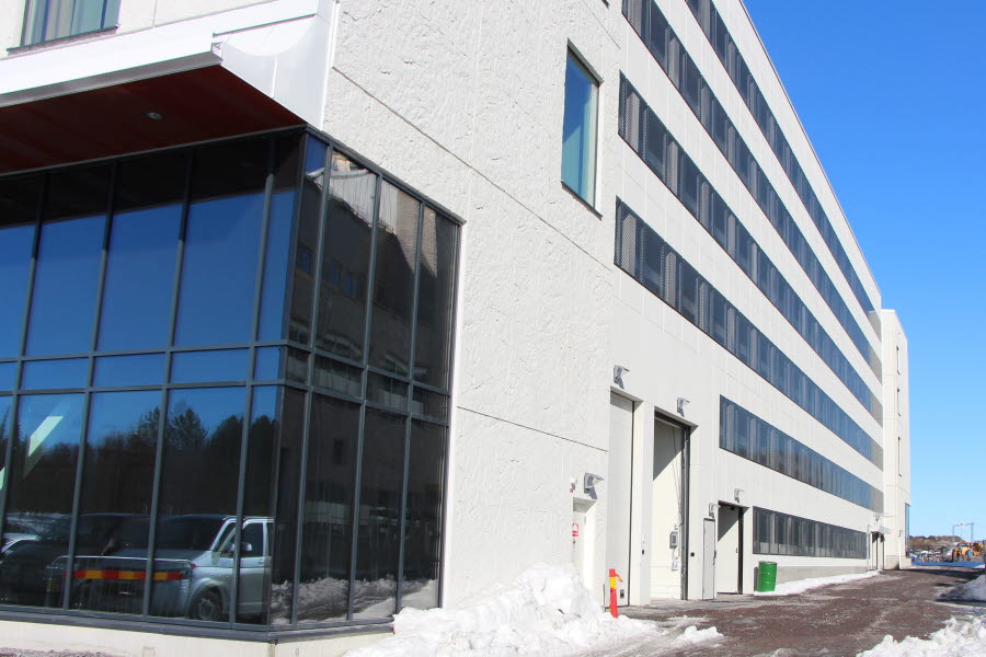Fotot visar en vit byggnad med infart till parkeringshuset.