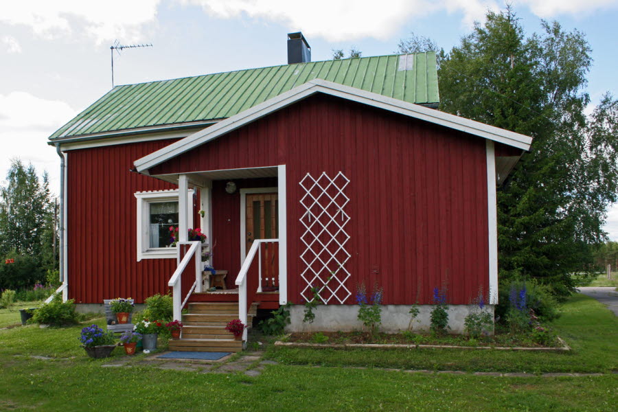 röd stuga i sommarmiljö med planeringar runt huset