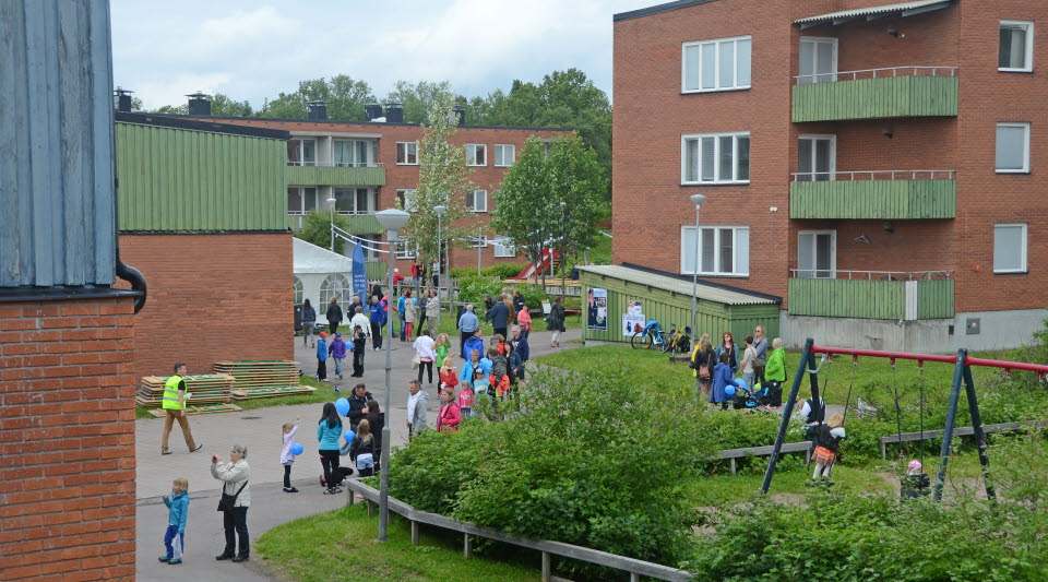 Människor bland tegelhus med gröna balkonger