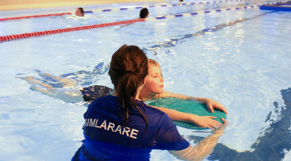 Barn som använder flytdyna med hjälp av simläraren för att lära sig att simma.