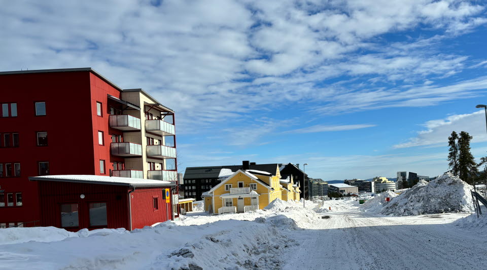 Fotot visar en väg med både flerfamiljshus och mindre trähus, med Kirunas stadskärna längst bort i bild.