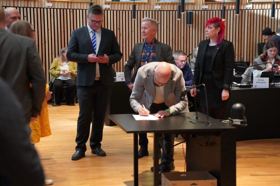 Krister Pounu skriver på uttalandet. I bakgrunden står Stefan Sydberg, Mats Taaveniku och Sanna Inga Poromaa. De befinner sig i kommunfullmäktiges sessionssal.
