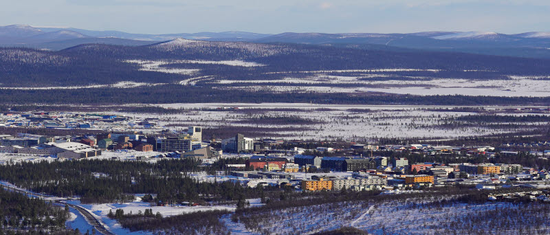 Stadsvy över ett snötäckt bostadsområde med flerbostadshus och villor i olika färger.