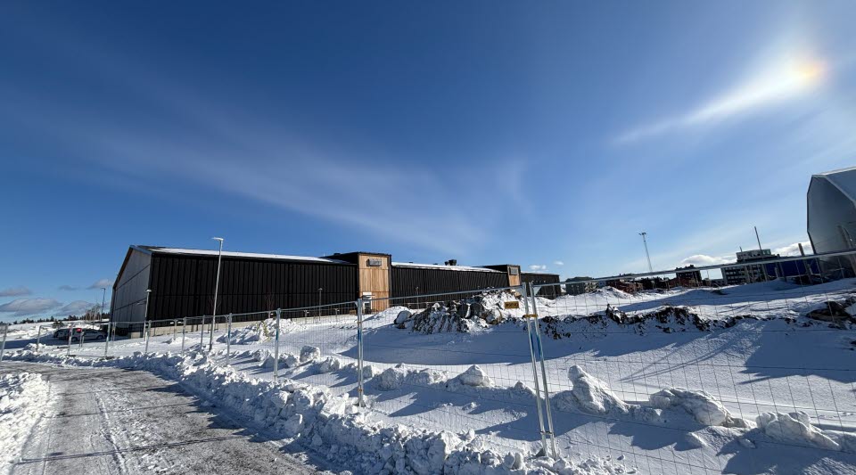 Fotot visar blå himmel och snö längs en gångväg med stängsel. 