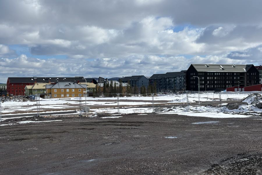 Fotot visar bostadshus i olika storlekar och färger. Längst fram på bilden ses ett byggstängsel framför ett tomt område. 