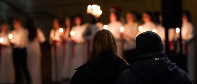 Ett luciatåg framför två personer.