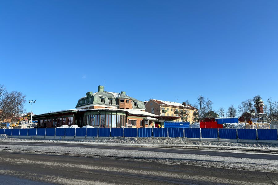 Fotot visar hus som rivs bakom ett stängsel mot en blå himmel. 