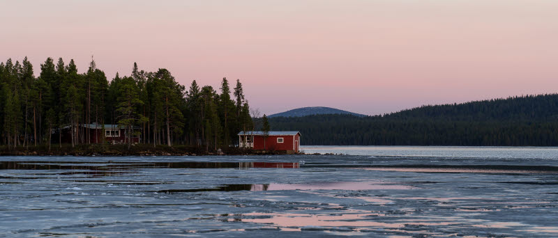 Isbrytning på Torneälv med två röda stugor i skogen i bakgrunden