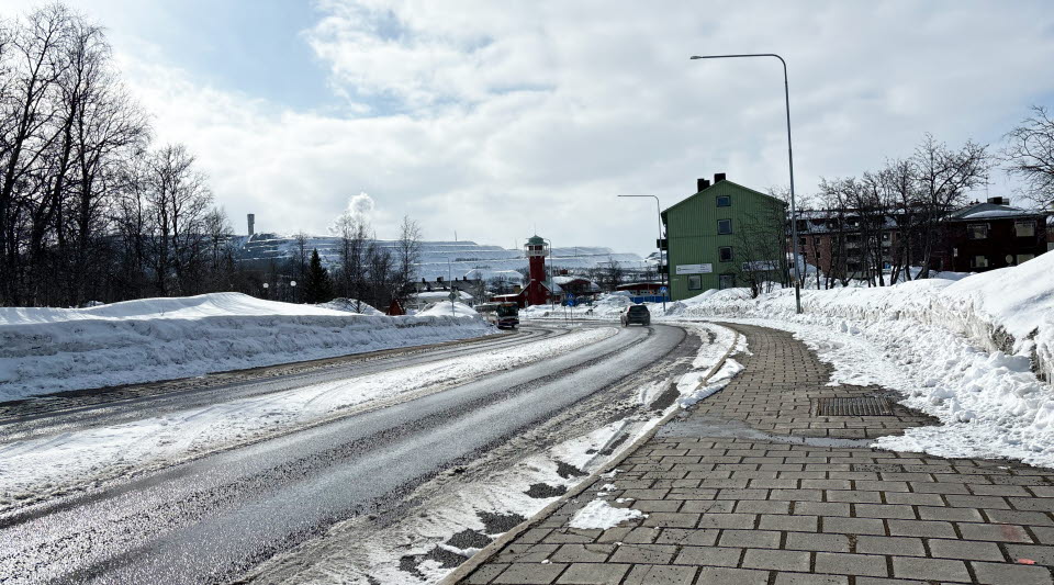 Fotot visar en väg med trottoarer och hus längre ner med gruvan i Kiruna i bakgrunden.