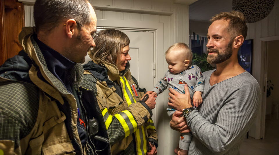 Två brandmän pratar med en pappa som har ett litet barn i famnen