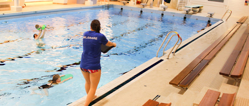 Simlärare står vid sidan av en bassäng och visar barn hur de ska simma.