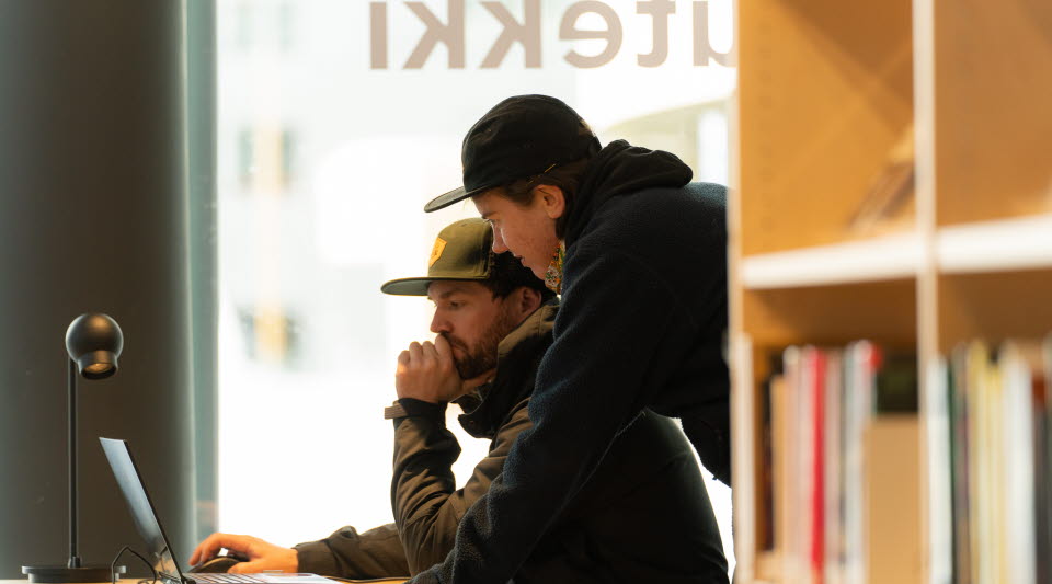 Två studenter som arbetar framför en dator i biblioteksmiljö