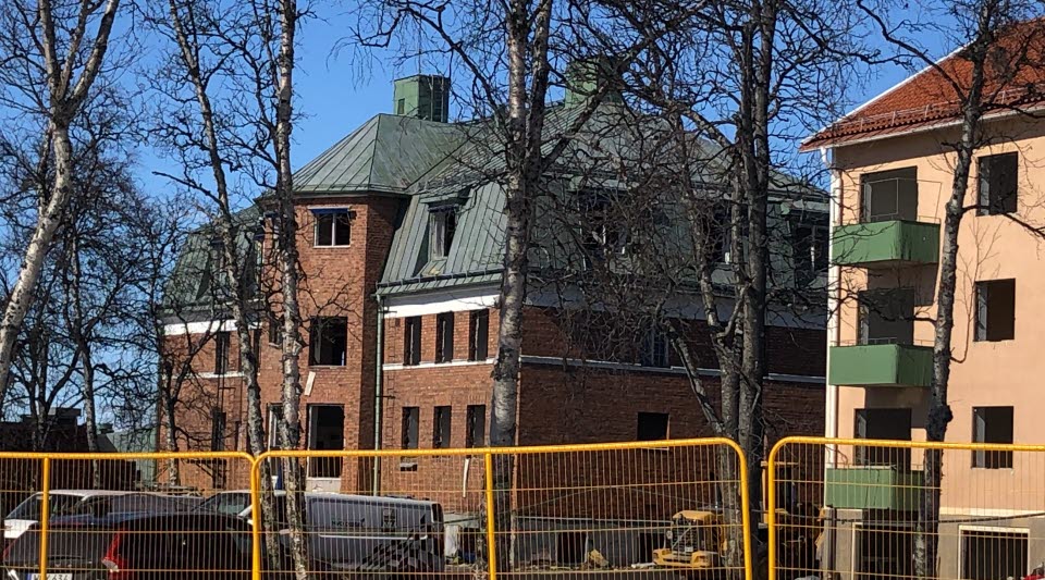 Fotot visar en visar en brun tegelbyggnad bakom ett gult industristängsel.