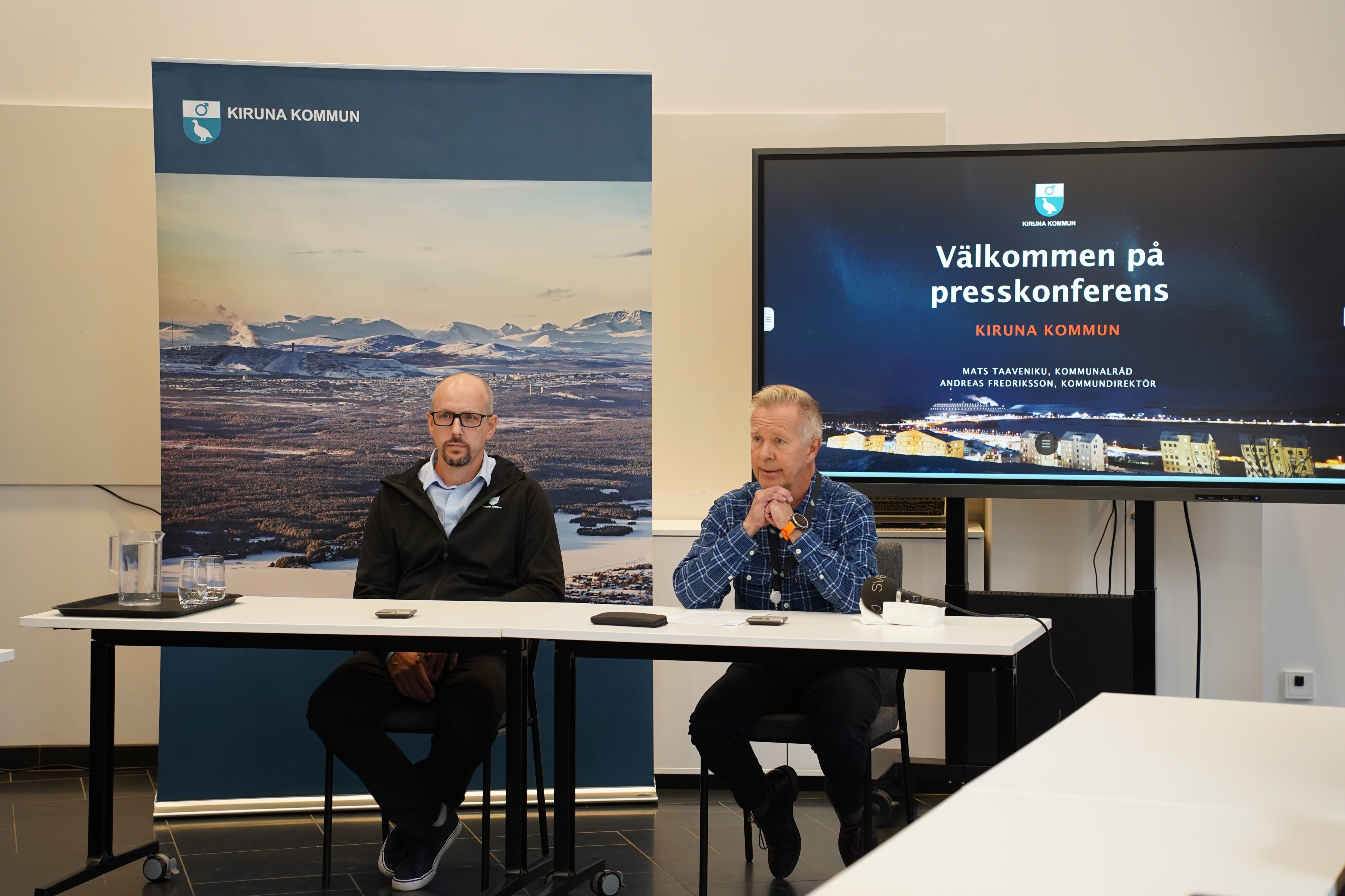 Kommundirektör Andreas Fredriksson och kommunalråd Mats Taaveniku på presskonferensen. De sitter framför en rollup och en skärm vid ett bord. 
