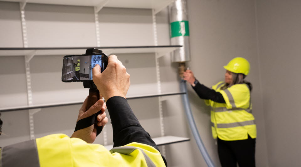 Fotot visar en person i varselkläder som vrider på en kran samtidigt som den blir fotograferad.