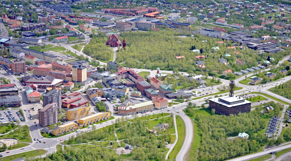 Kiruna centrum omgivet av grönska med kyrkan och kyrkoskogen synliga i mitten, vy över stadsmiljö, flygfoto.