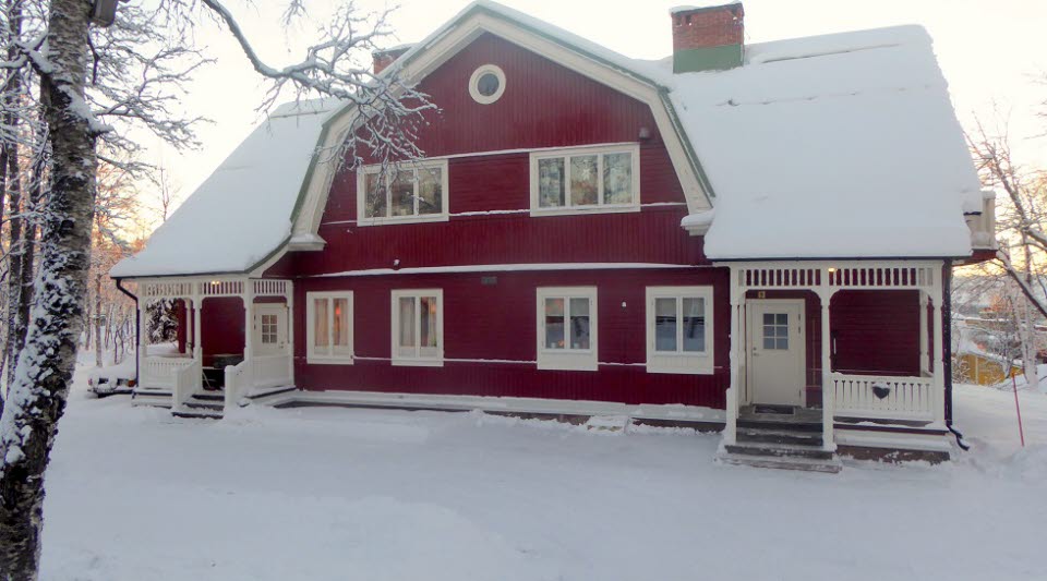 Fotot visar en röd träbyggnade med två likadana ingångar vintertid. 