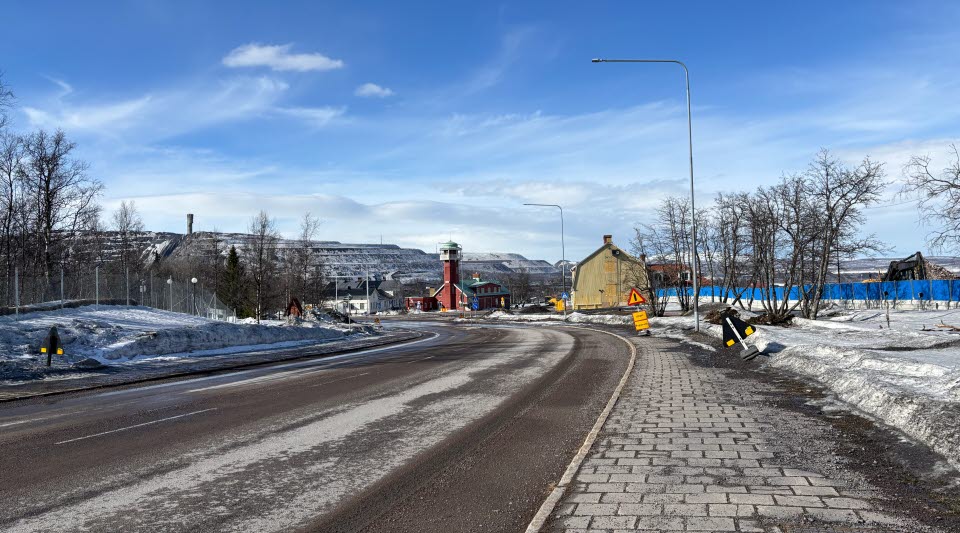 Fotot visar en gata, byggnader bakom byggstängsel och längst bak i bilden ett berg.