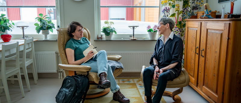 Fotot visar två personer som sitter och samtalar i ett rum.