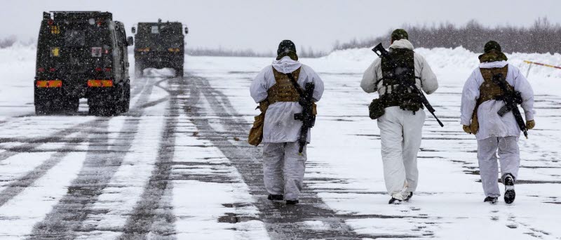 Tre soldater går längs en väg och i anslutning till en militärtransport.