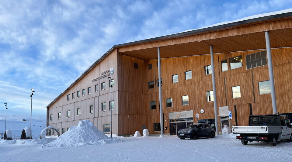 Fotot visar en brun byggnad på vintern med en blå himmel bakom.