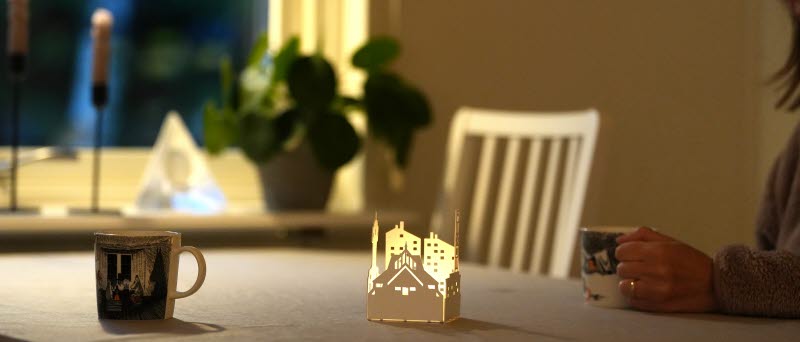 En hand håller i en kopp vid ett matbord med en ljuslykta och ytterligare en kopp.