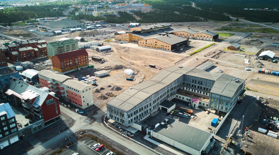 Fotot är taget på sommaren och visar en grå byggnad som är det nya polishuset tillsammans med andra hus i nya centrum. 