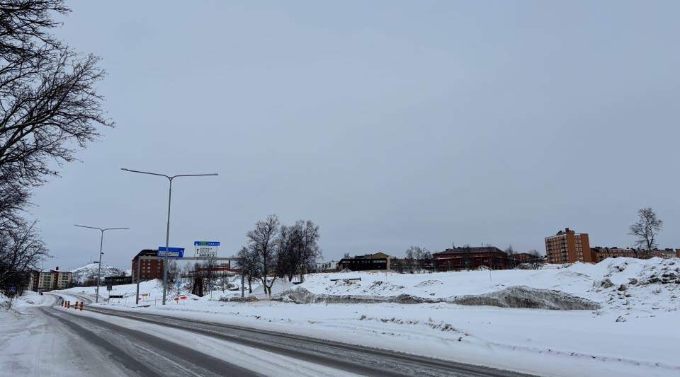 Fotot visar en väg med snötäckt mark och enstaka hus på ena sidan. 