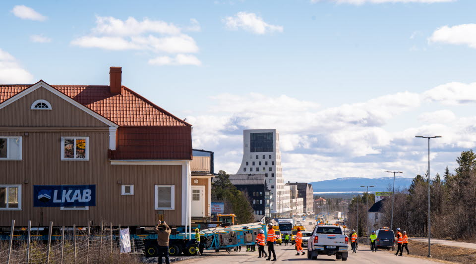 Beige hus på trailer mitt på en bilväg.