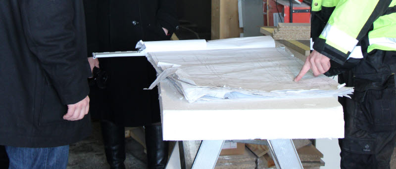 Tre personer står och kollar på en byggritning